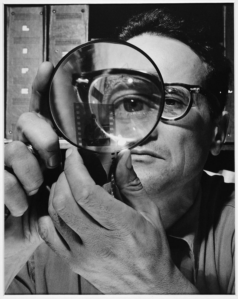 Die schwarz-weiß Fotografie zeigt ein inszinniertes Selbstporträt von Andreas Feininger, bei dem er mit einer Lupe eines seiner Augen vergrößert darstellt.
