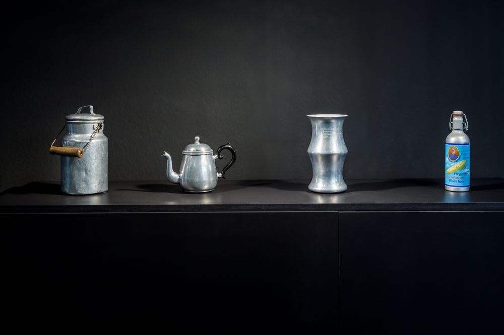 Die Ausstellungsansicht zeigt zwei Kannen, eine Vase und eine Bierflasche aus Aluminium.