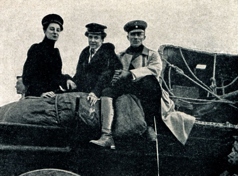 Die historische Fotografie zeigt zwei Frauen und einen Mann, die auf einer Erhöhung sitzen. Rechts neben dem Mann liegt ein Ballonkorb. 