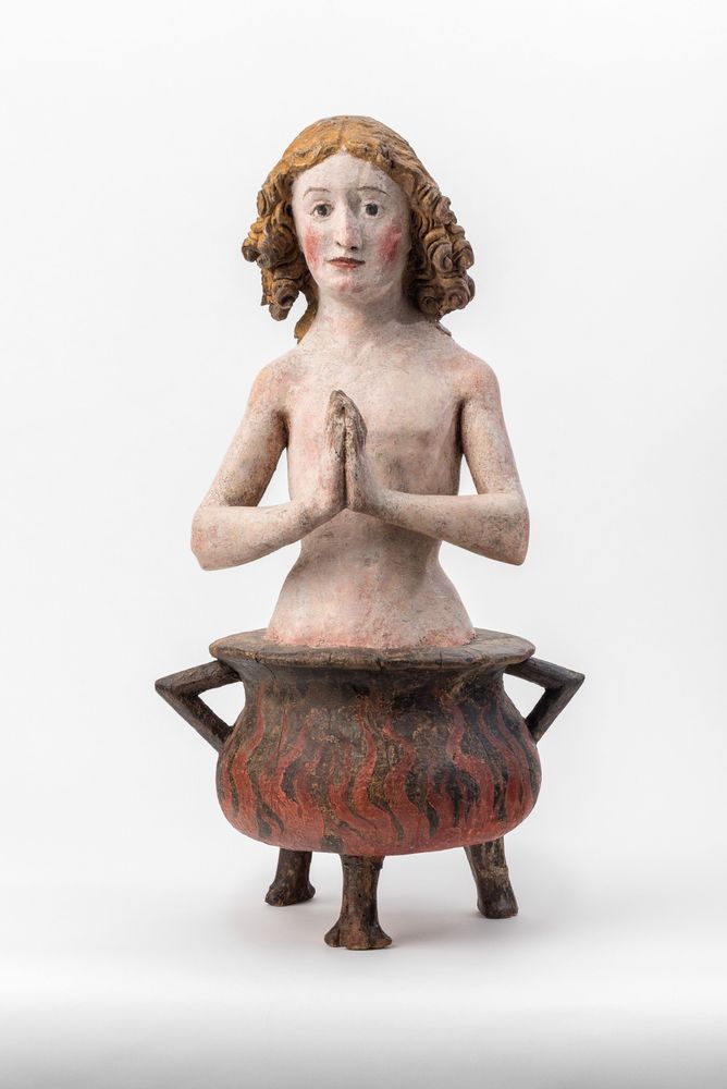 Die Aufnahme zeigt die Skulptur eines Jungen der mit betenden Händen in einem brennenden Kessel sitzt..