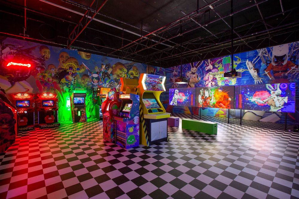 Installationsansicht mit verschiedenen Spielautomaten wie in einer Arcade. Der Boden hat ein Schachbrettmuster.