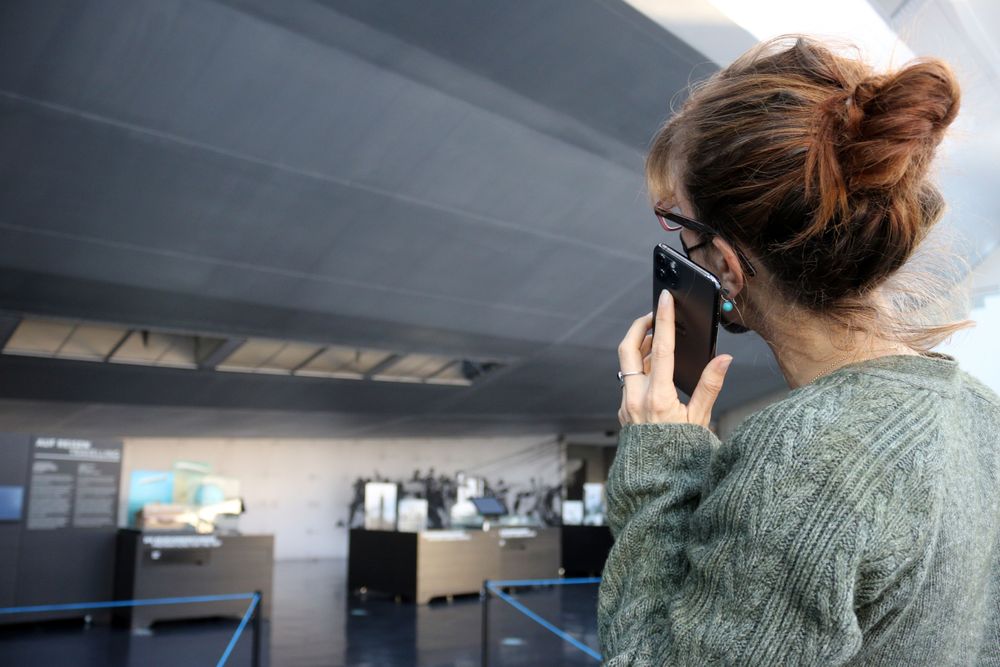 Eine Frau hält sich ein Smartphone ans Ohr und betrachtet die Teilrekonstruktion der Hindenburg.