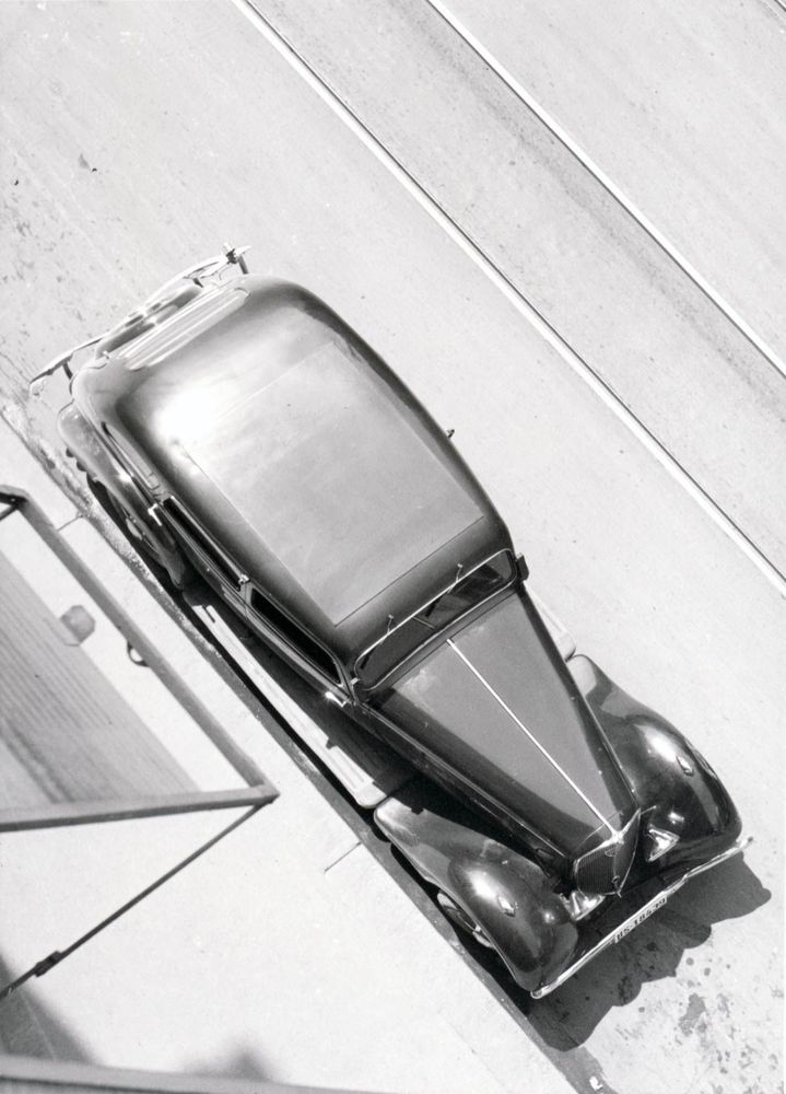 Die schwarz-weiß Fotografie zeigt eine alte Limousine aus der Vogelperspektive fotografiert.