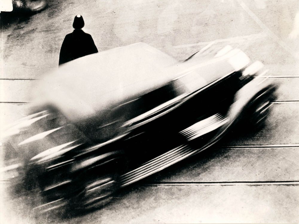 Die schwarz-weiß Fotografie zeigt ein verschwommenes Auto, welches während der Aufnahme in Bewegung war.