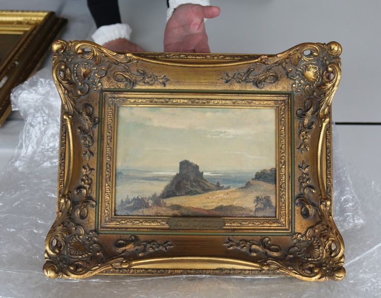 Die Aufnahme zeigt ein Gemälde in einem prunkvollen Rahmen. Eine Hand hält den Rahmen von unten und hält das Gemälde in die Kamera.