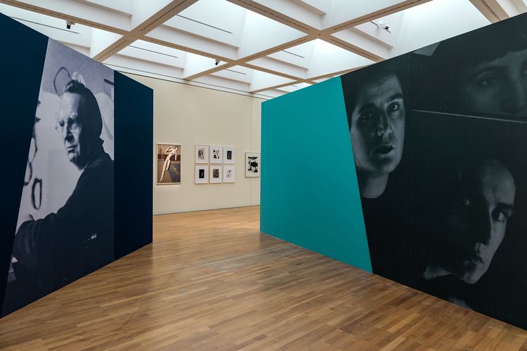 Die Ausstellungsansicht zeigt zwei breite Wände, die im Raum aufgestellt sind. An der vorderen Wand ist ein großes Porträt von Willi Baumeister abgedruckt. Auf der Wand daneben drei Porträtaufnahmen von Marta Hoepffner. 