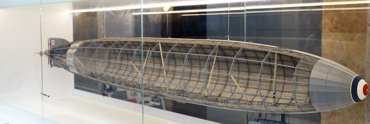 Modell eines Zeppelins in einer Glasvitrine, mit sichtbarem Gerüst und detaillierter Innenstruktur. Die Spitze des Luftschiffs zeigt eine runde Markierung in Blau, Weiß und Rot.