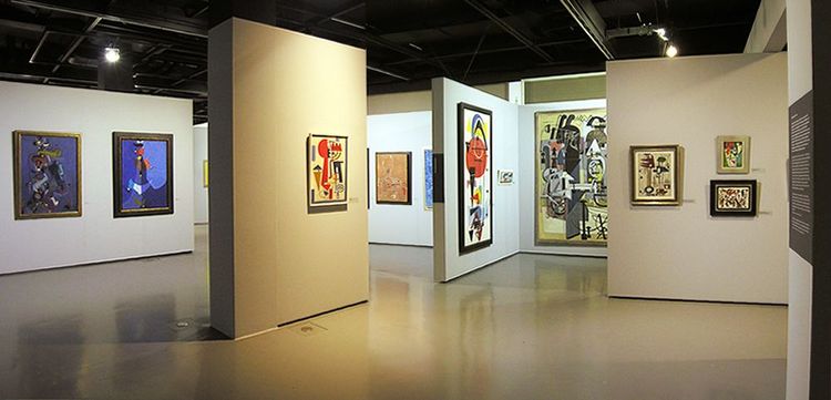 Raumansicht der Ausstellung mit mehreren Trennwänden, an denen verschiedene Gemälde und Zeichnungen hängen.