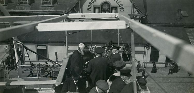 Graf Zeppelin, Prinz Heinrich von Preußen, Expeditionsteilnehmer und Gäste auf dem Dampfer „Mainz“. Im Hintergrund steht ein Gebäude mit dem Schriftzug „Norddeutscher Lloyd“. 