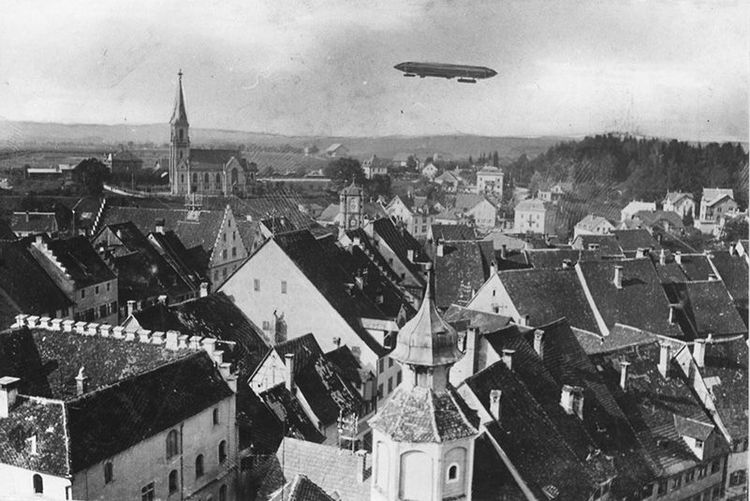 LZ 2 über Wangen. Schwarz-weiße Fotomontage des Fotografs Franz Walchner. Man sieht die Dächer von Wangen im Vordergrund, mit der Kirche im linken Bildmittelgrund. Rechts vom Kirchturm fährt der Zeppelin. 