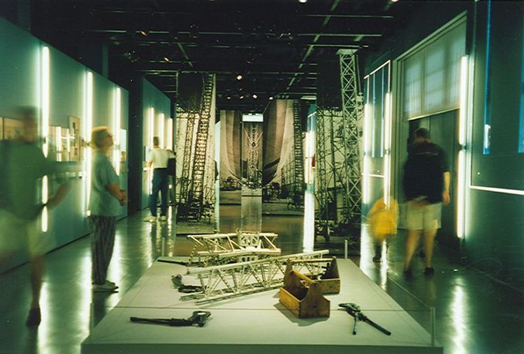 Die Ausstellungsansicht von "Zirkel, Zangen und Celon" zeigt einen Flur, in dem sich auf beiden Seiten verschiedene Exponate befinden. In der Mitte auf einem Tisch liegen verschiedene Werkzeuge.
