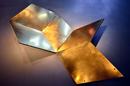 Auf dem Boden befindet sich eine geometrische Installation aus metallischen Platten, die miteinander verbunden sind.