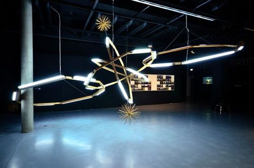 Von der Decke eines dunklen Raumes hängt eine große leuchtende Installation, die unter anderem aus Leuchtstoffröhren besteht.