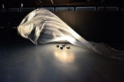 Eine leuchtende Installation, bestehend aus durchsichtiger, drapierter Folie befindet sich in einem dunklen Raum.