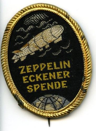 Anstecknadel mit gesticktem ovalem Bild. Oben fährt der Zeppelin durch die Wolken, unten sieht man einen Teil der Weltkugel, mittig steht: Zeppelin Eckener Spende. 