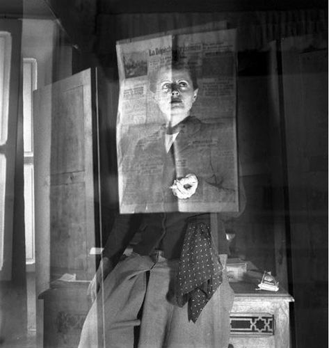 Die schwarz-weiß Fotografie zeigt ein Selbstporträt der Künstlerin Ré Soupault. Sie lehnt an einem kleinen Tisch und schaut in die Ferne. In der Hand hält sie eine Zigarette. Über ihrem Kopf und dem Oberkörper spiegelt sich ein Zeitungsblatt.