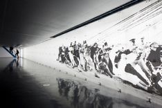 An einer hell leuchtenden weißen Wand ist ein schwarz-weiß Foto einer Haltemannschaft abgebildet. Die Männer auf dem Bild sind in gebeugter Haltung und halten an verschiedenen Seilen fest.