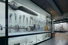 Ausstellungsansicht einer großen Glasvitrine, die hell beleuchtet ist. In der Vitrine befinden sich mehrere Zangen und eine Art großer Propeller oder Schraube.