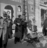 Die schwarz-weiß Fotografie zeigt eine Gruppe von Musikern, die auf der Straße spielen. 