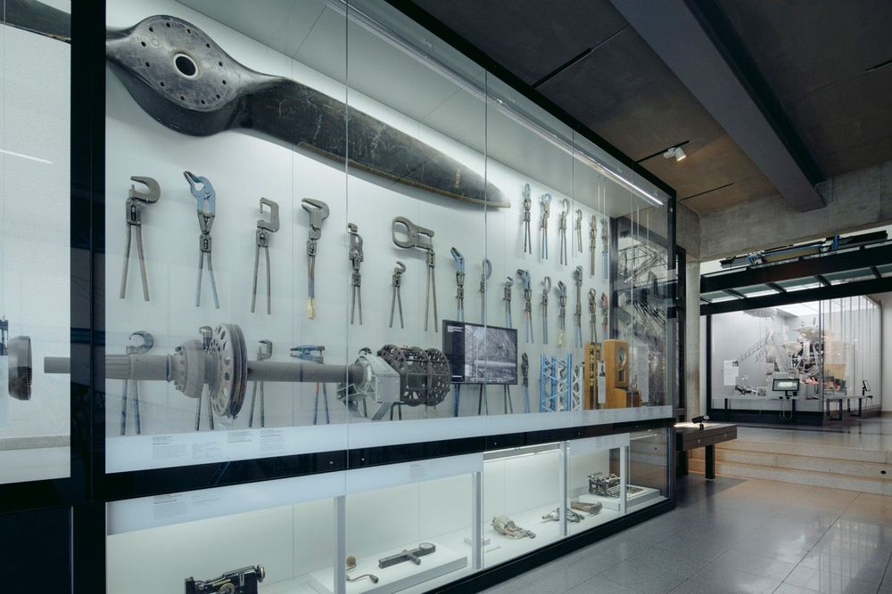 Ausstellungsansicht einer großen Glasvitrine, die hell beleuchtet ist. In der Vitrine befinden sich mehrere Zangen und eine Art großer Propeller oder Schraube.