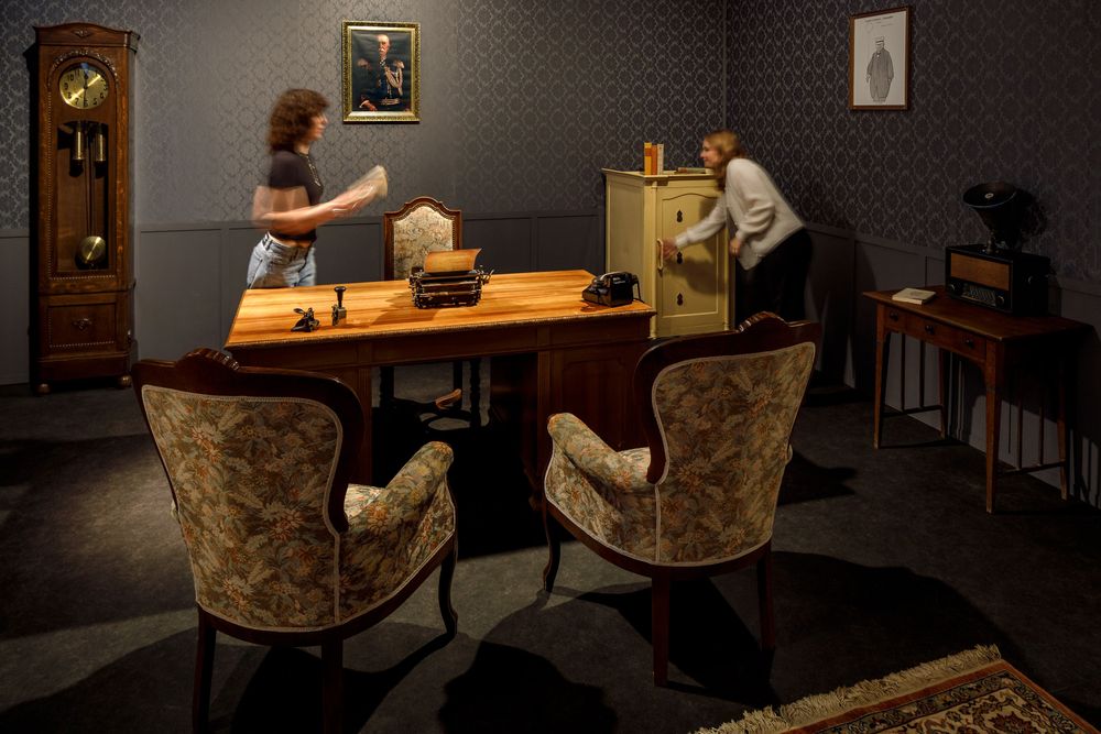 Zwei Personen spielen im Escape Room vom Zeppelin Museum. Das ist ein Bürozimmer mit alten Möbeln.
